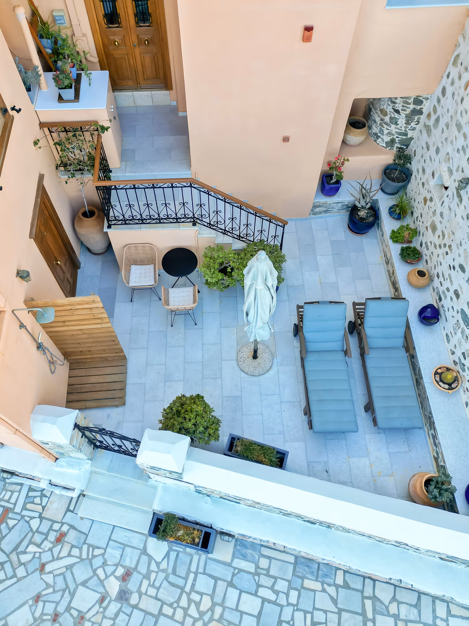 Bird's-eye view of a patio with two chaise lounges, two chairs, plants, and a closed umbrella.