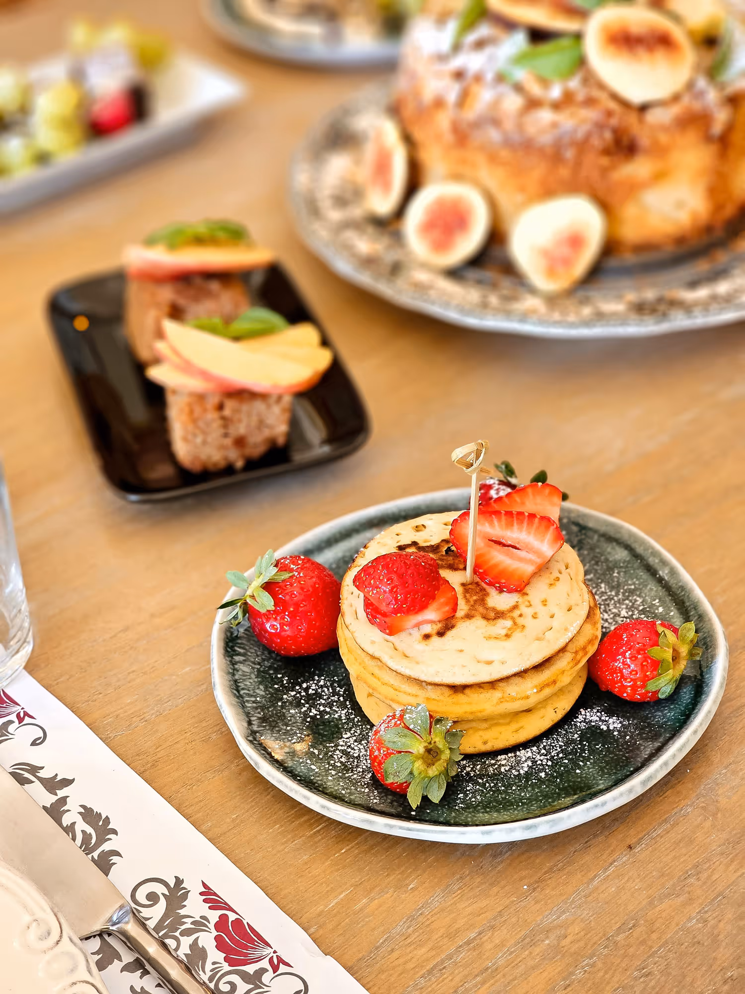 Stack of pancakes topped with sliced strawberries and surrounded by whole strawberries on a dark green plate.