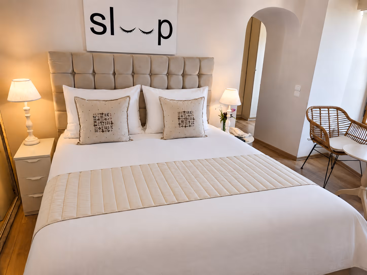 Modern bedroom with beige tufted headboard, white bedding, two beige pillows, and lamps on each side.