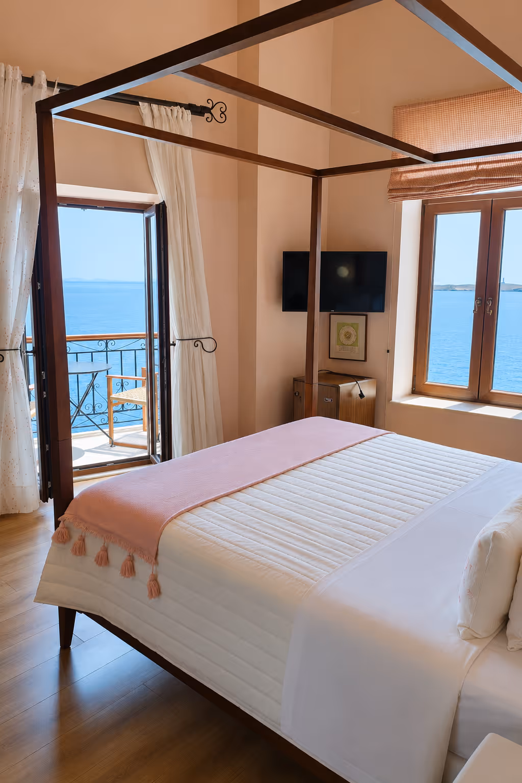 Bedroom with four-poster bed, white linens, pink throw, and balcony overlooking the ocean.