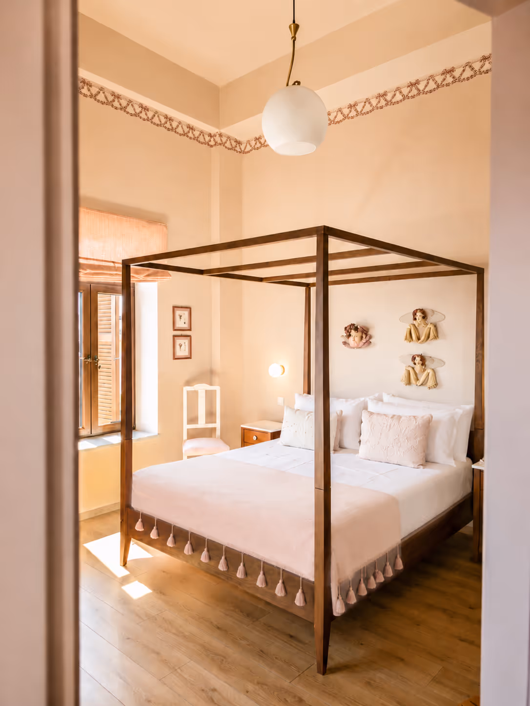Light bedroom with wooden four-poster bed, white bedding, decorative pillows, and wall art above headboard.