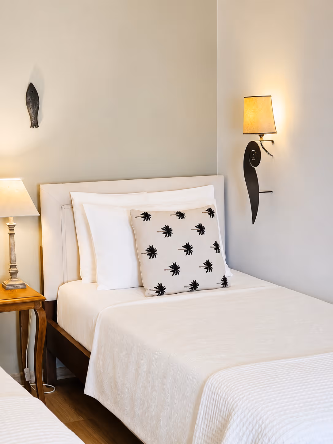 Bed with white linens and a pillow with black palm tree patterns in a softly lit room.