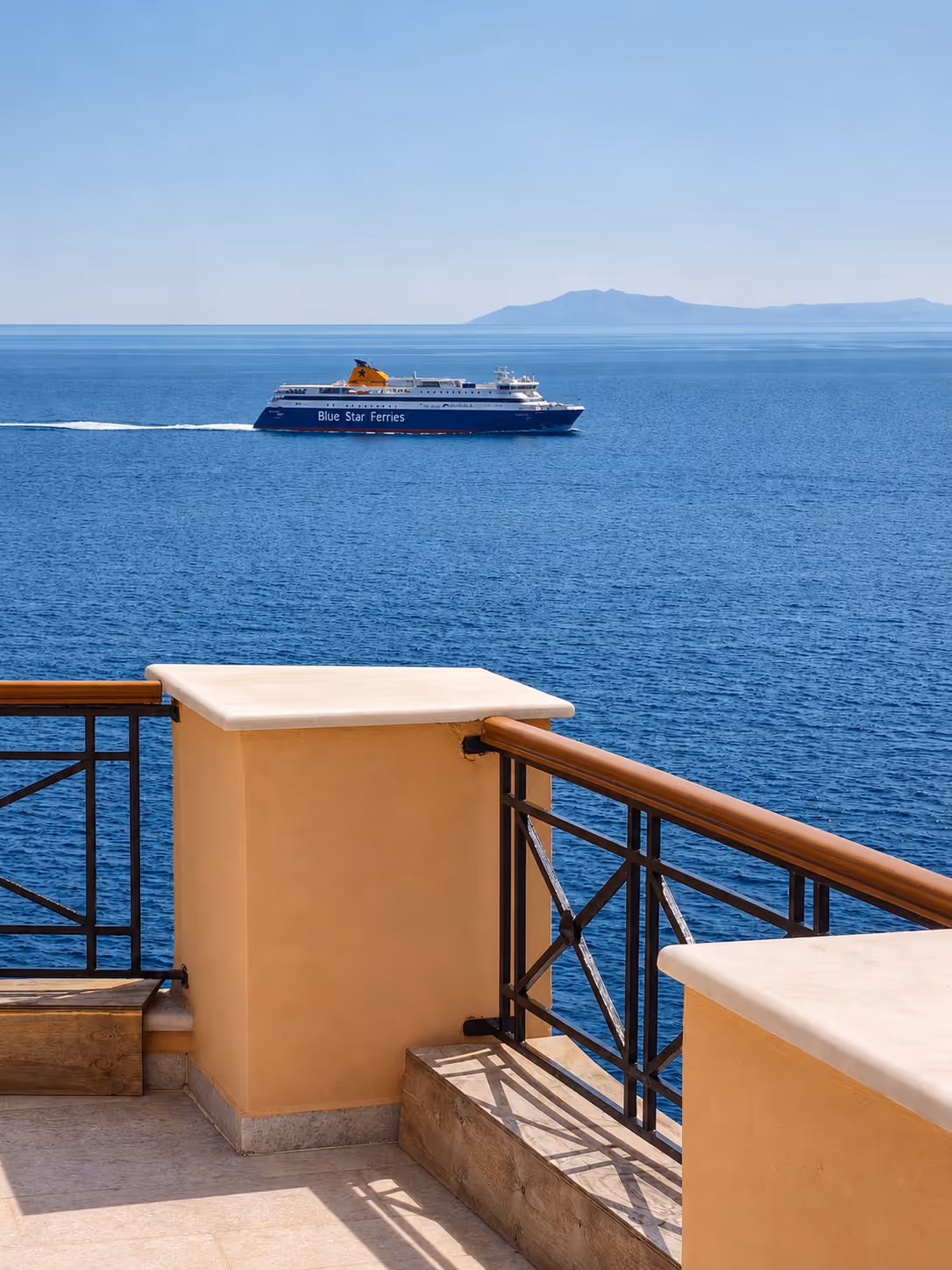 Blue Star Ferries ship sailing on calm blue sea seen from sunny terrace with railings.