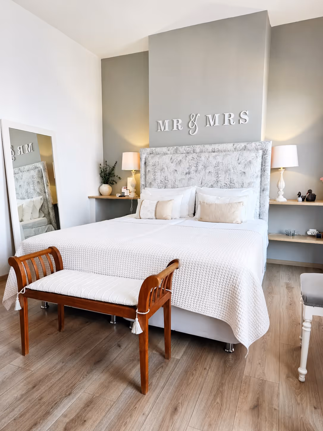 Bedroom with a white king bed, patterned headboard, wood bench, and wall letters spelling MR & MRS.