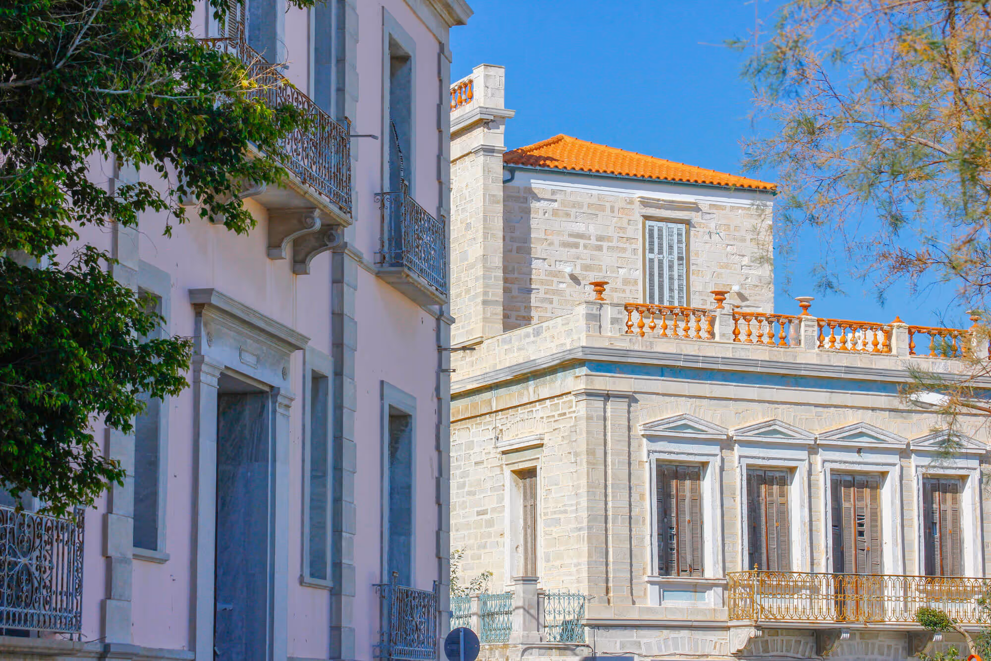 Two adjacent Mediterranean-style buildings with wrought iron balconies under a clear blue sky.