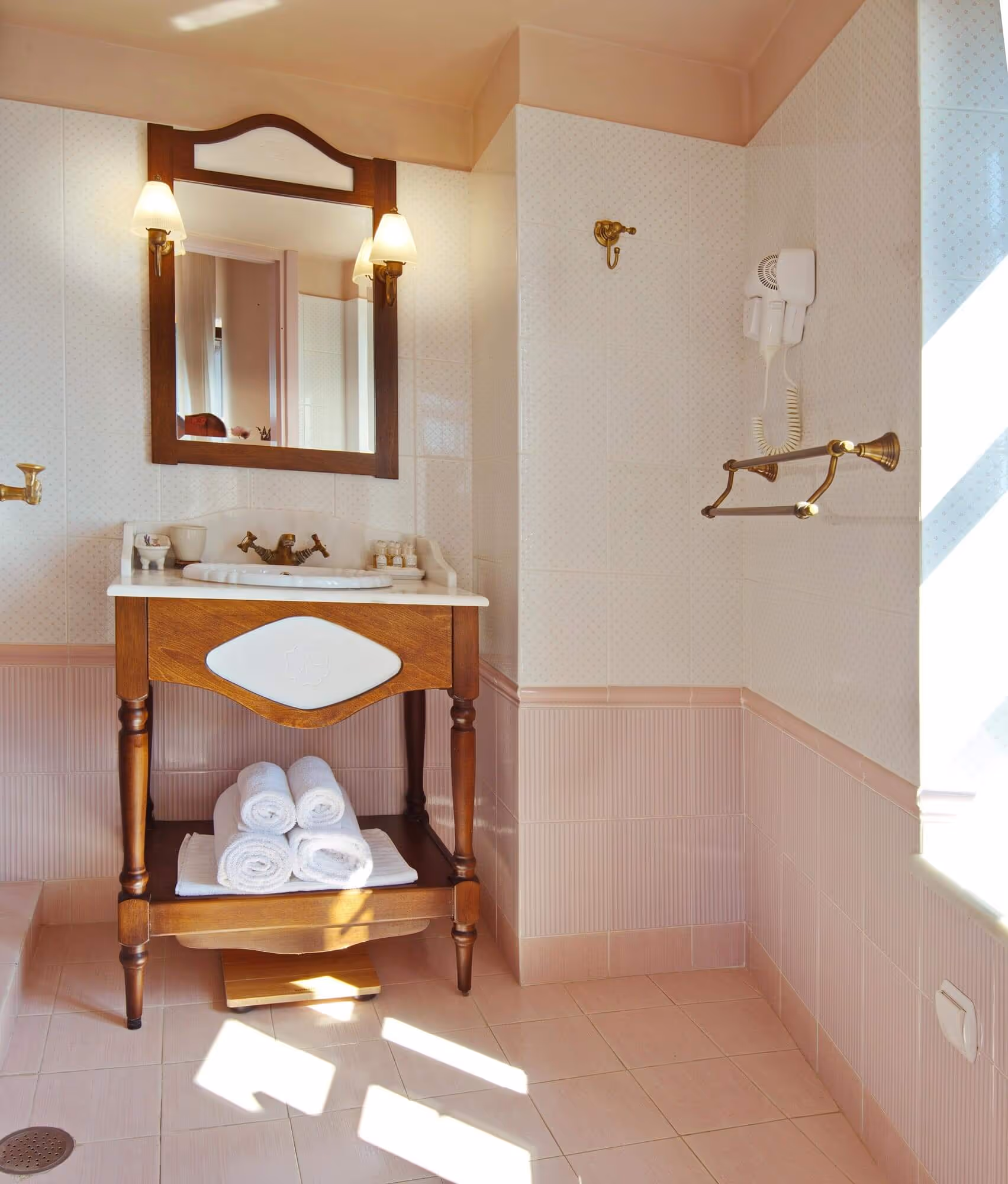 Vintage-style bathroom sink with wooden cabinet, mirror with lights, and rolled white towels beneath the sink.